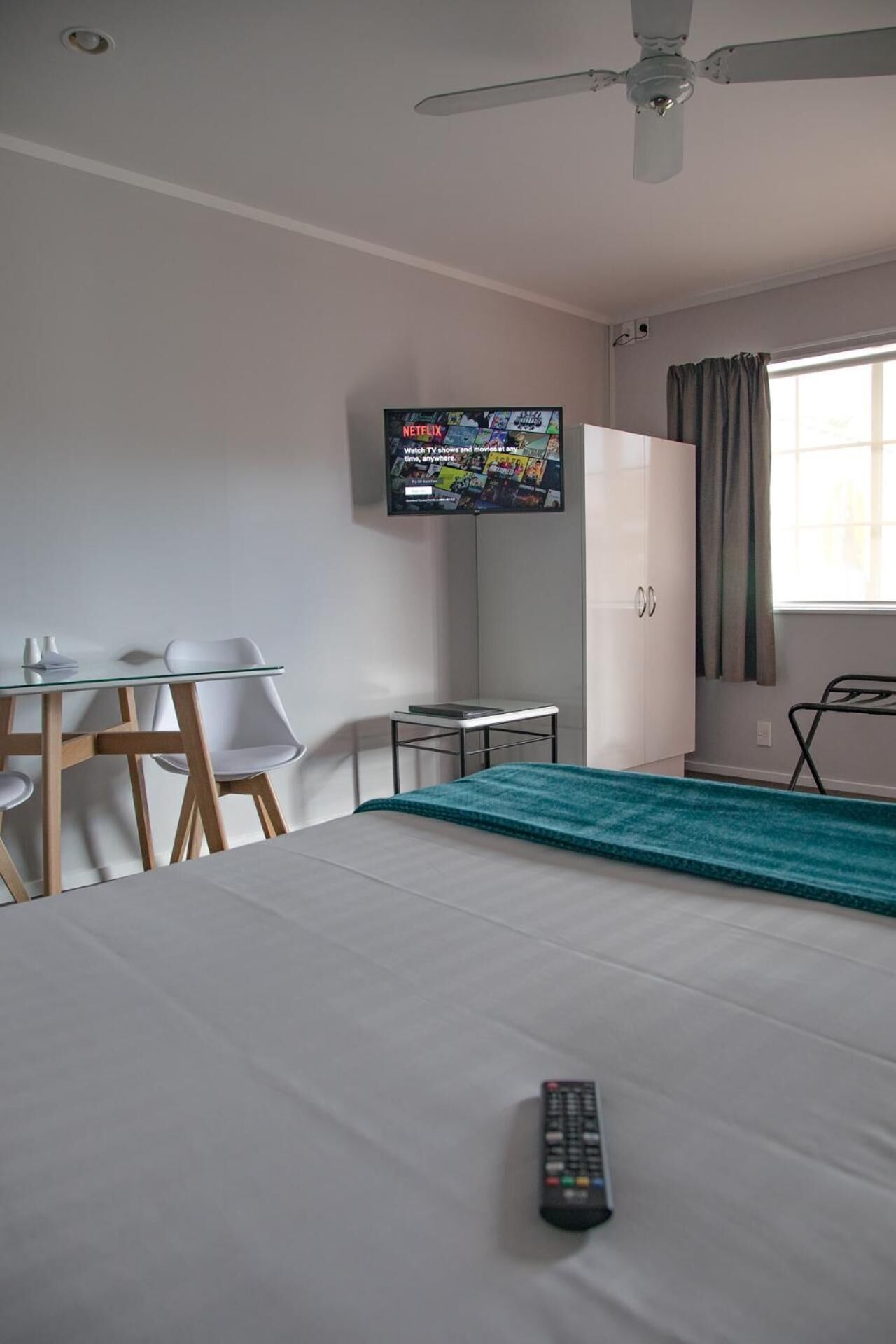 A hotel room with a bed, a TV mounted on the wall, a desk with chairs, and a window with curtains.