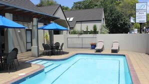 A swimming pool with lounge chairs and umbrellas, a covered seating area, and a sign for Bethlehem Motor Inn. - Bethlehem Motor Inn (Tauranga)