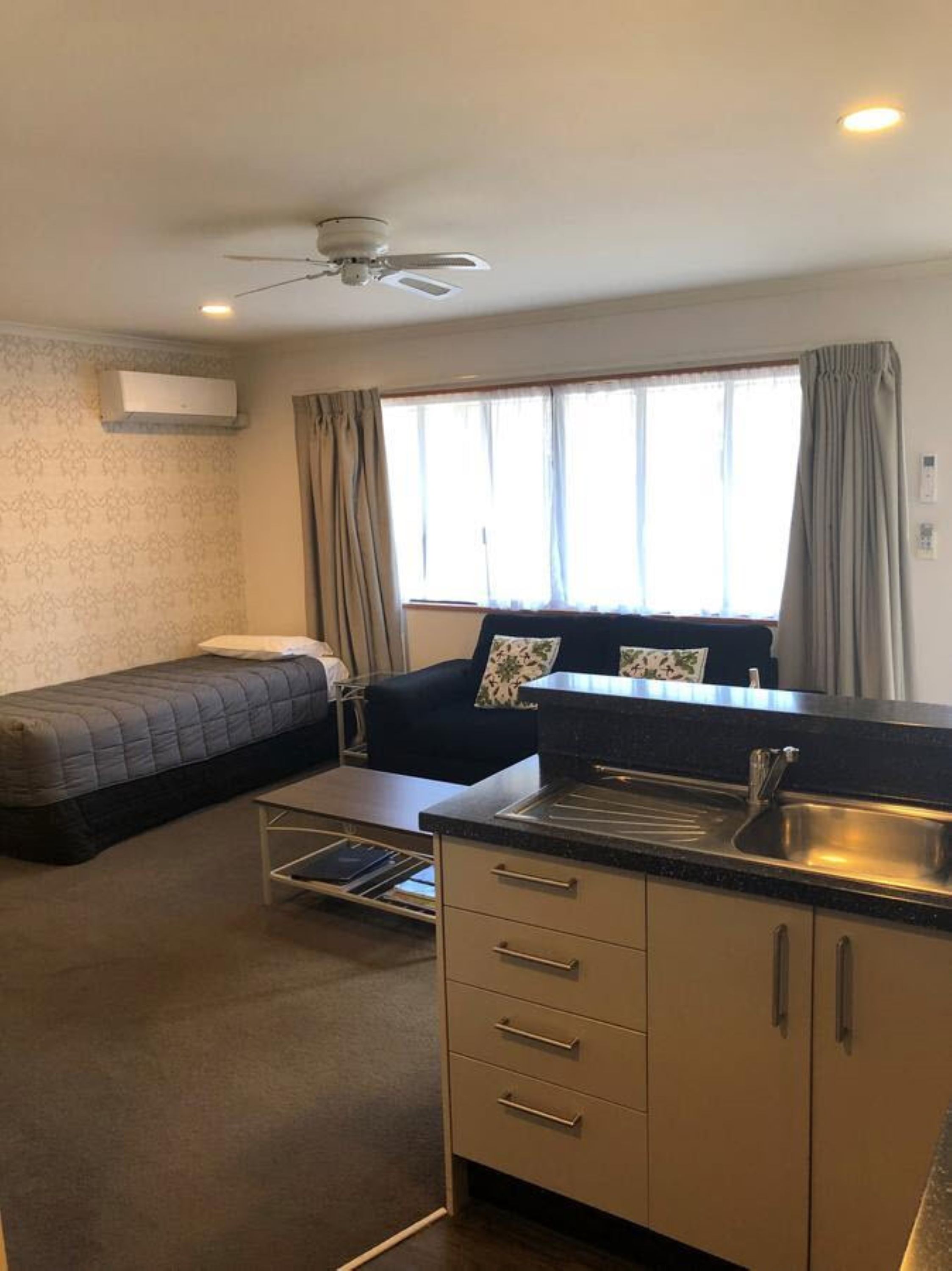 Habitación compacta con cama, sofá, kitchenette y ventilador de techo.