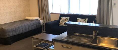Habitación compacta con cama, sofá, kitchenette y ventilador de techo.