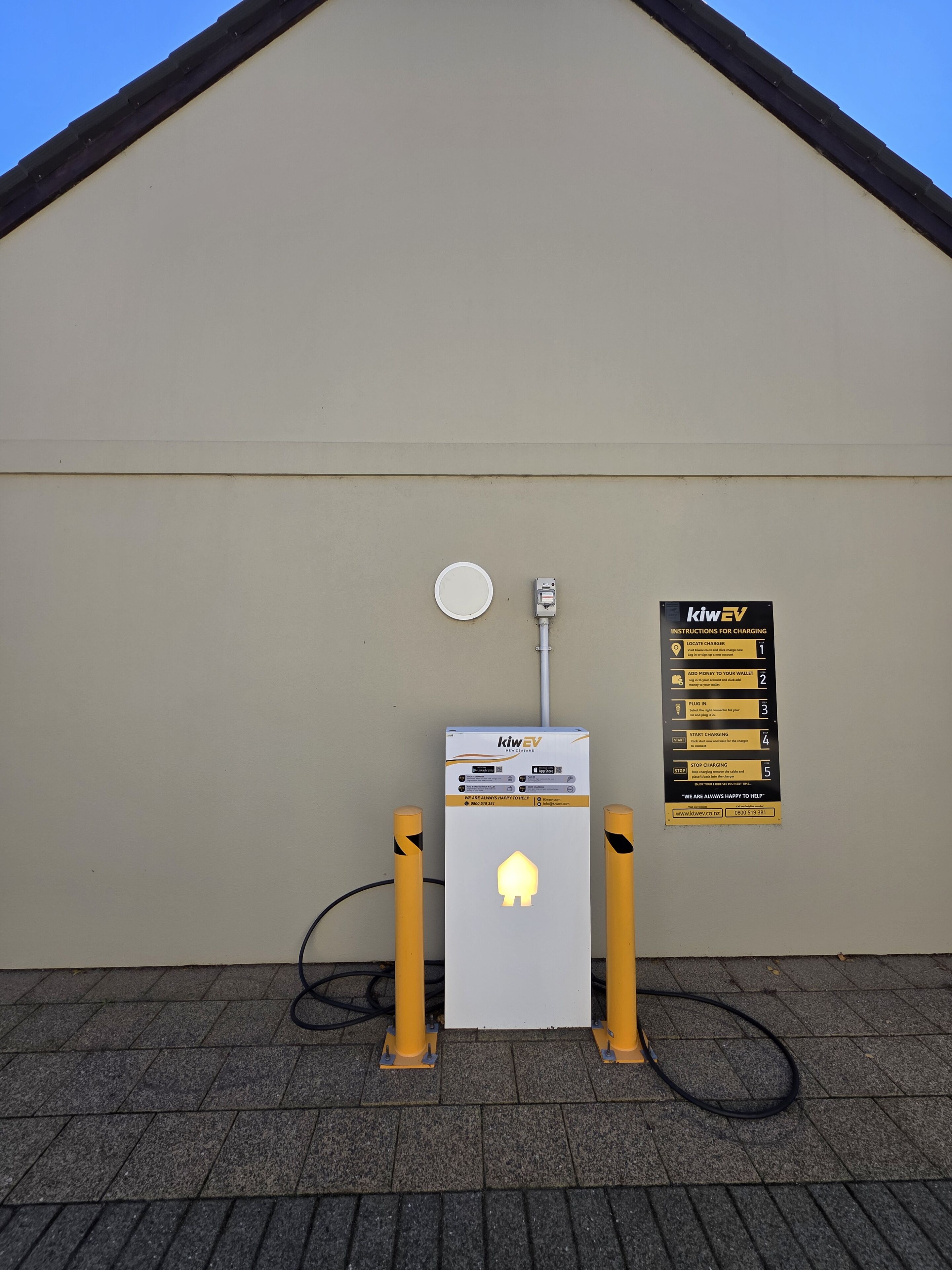 Une borne de recharge dotée d’un panneau explicatif décrivant le processus de recharge, d’une prise de courant et d’un câble relié à la borne.