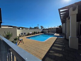 Um quintal com piscina, móveis de pátio e uma pérgola.