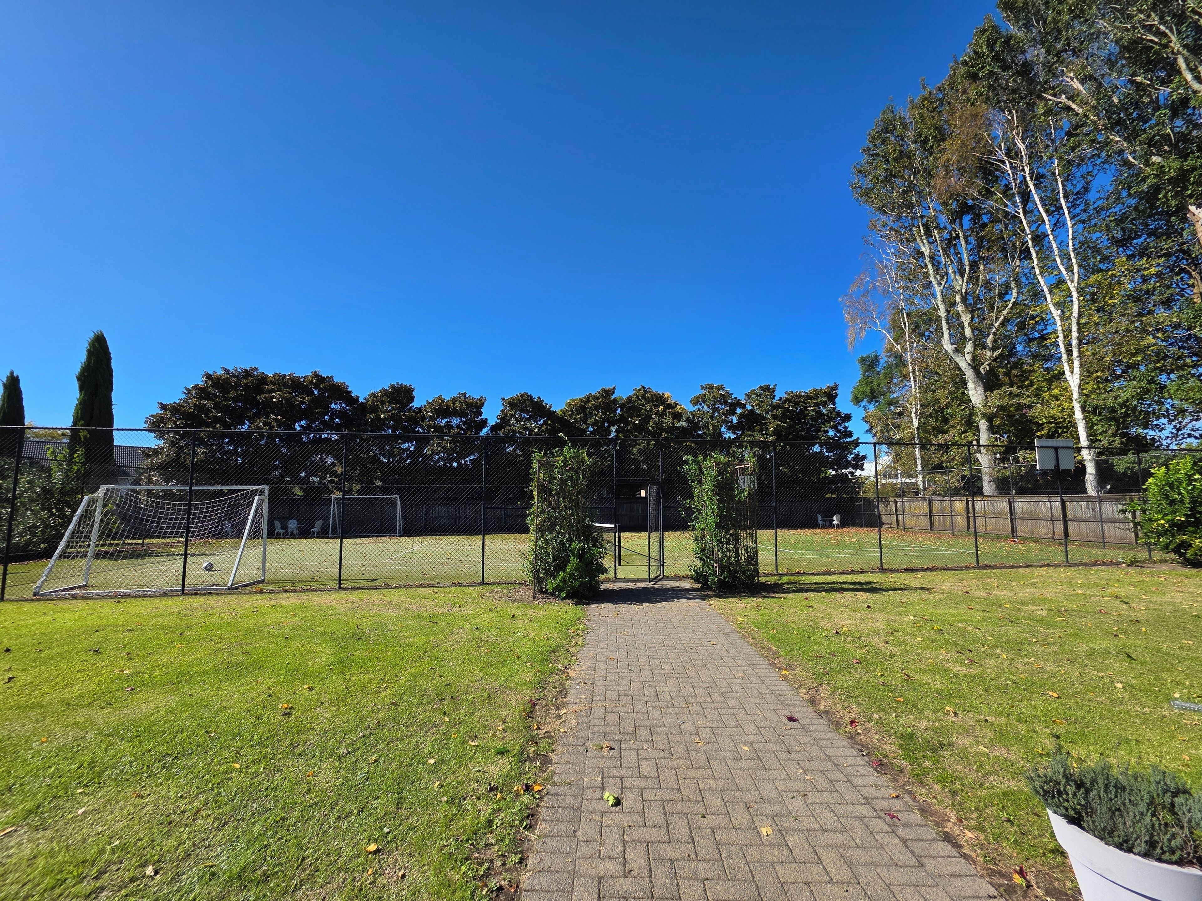 A paved pathway leading to a fenced sports field with a goalpost.