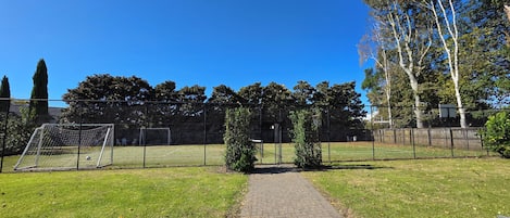 A paved pathway leading to a fenced sports field with a goalpost.