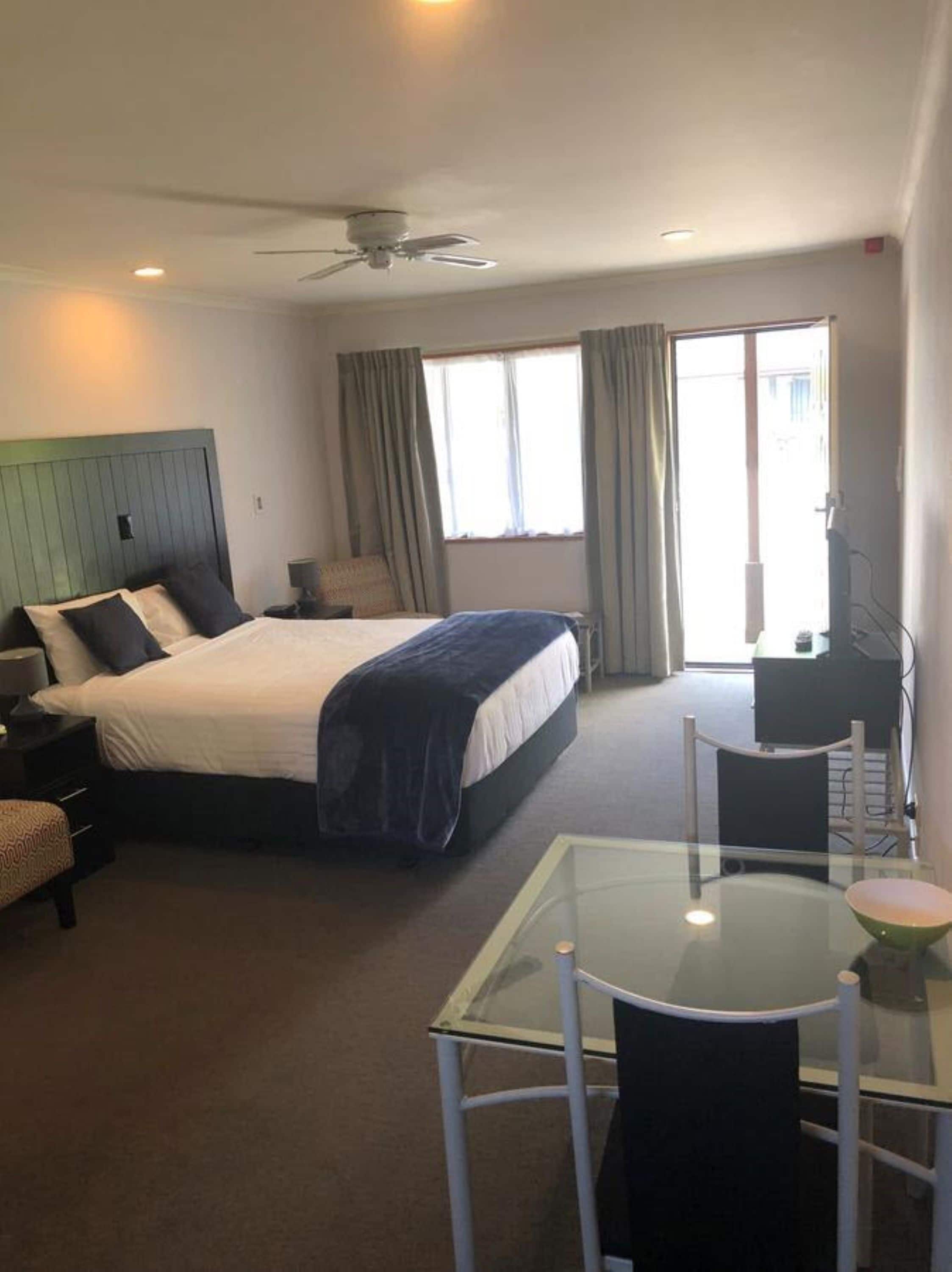 Habitación de hotel con cama, escritorio, silla, ventilador de techo y ventana.