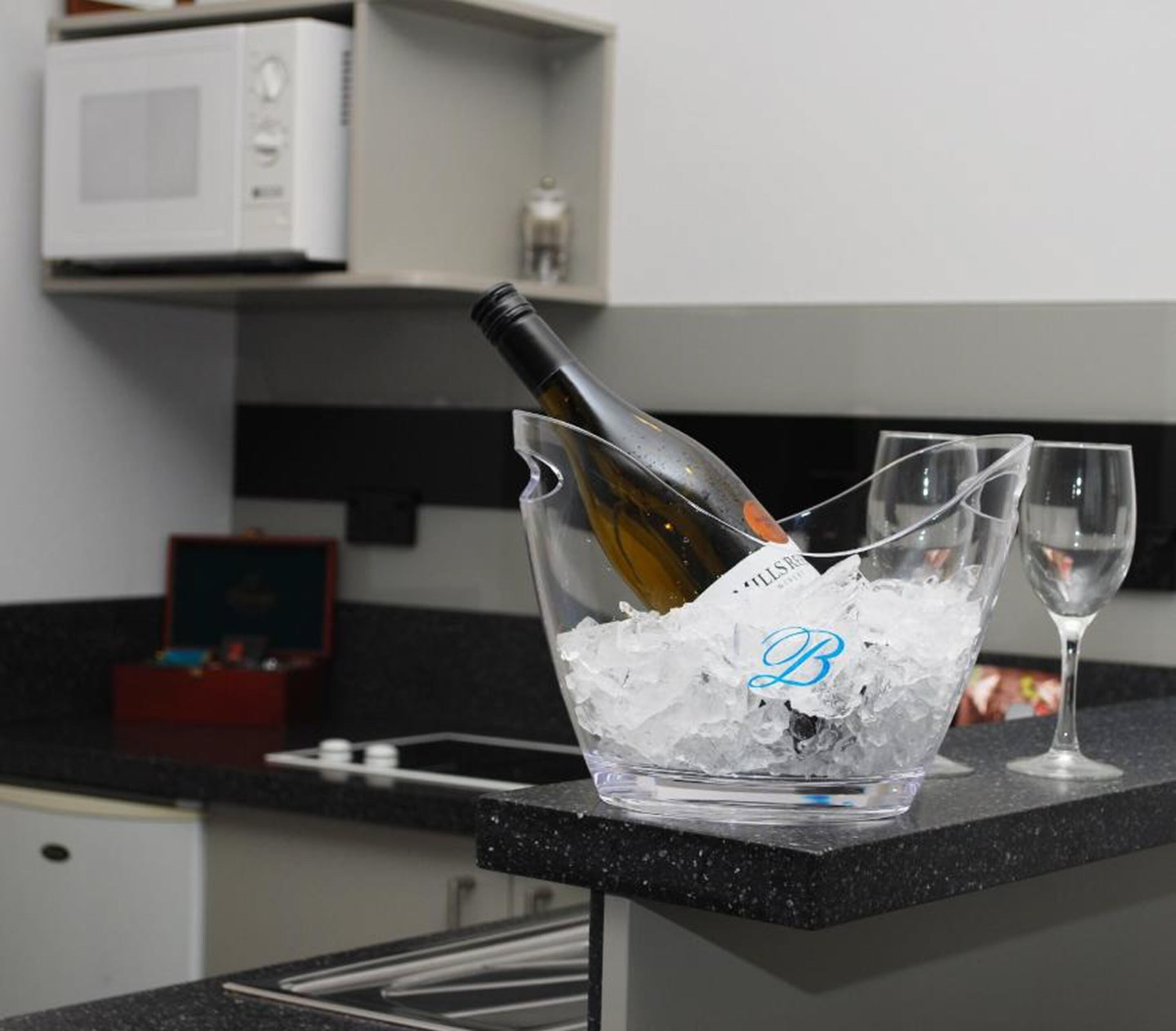 Un piano di lavoro della cucina con una bottiglia di vino in un contenitore trasparente pieno di ghiaccio, un bicchiere da vino e un forno a microonde sullo sfondo.