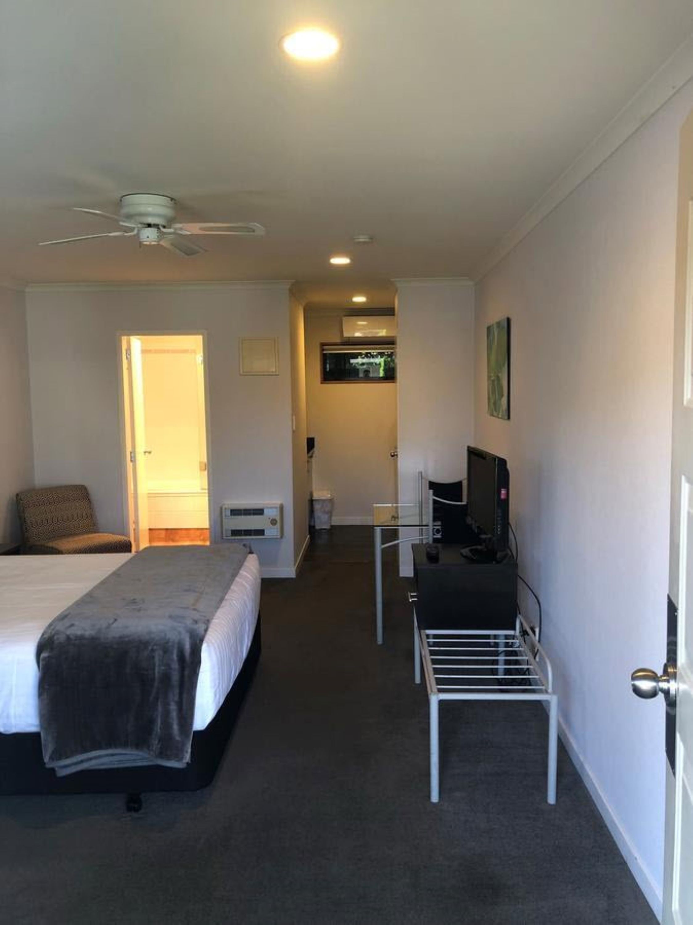 A hotel room with a bed, a desk with a computer, a chair, a TV, and a ceiling fan.