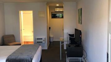 Habitación de hotel con cama, escritorio con computadora, silla, televisor y ventilador de techo.