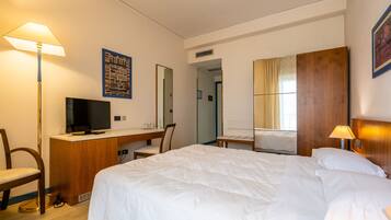 Habitación de hotel con cama, escritorio, silla, televisor y espejo.