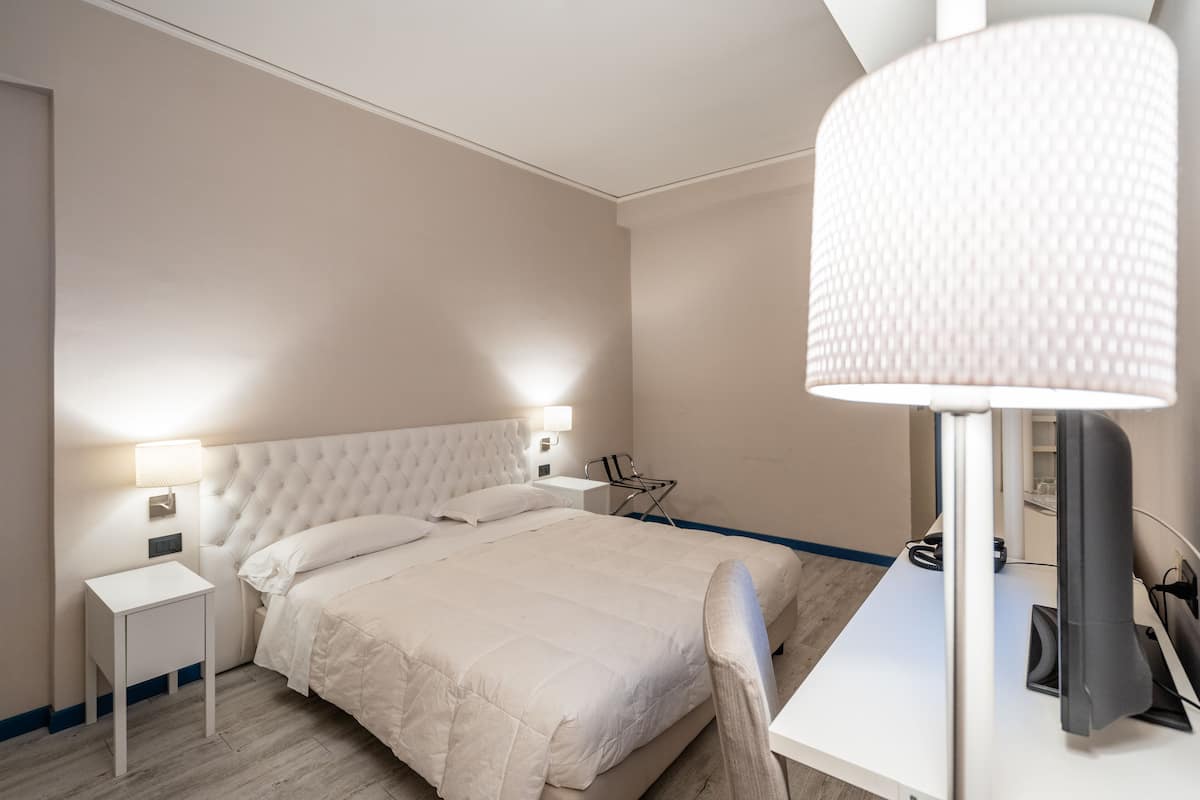 A neatly arranged bedroom with a large bed, bedside tables, a desk, and a lamp.