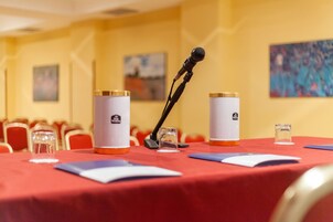 Un salón de conferencias con una mesa roja, micrófonos y botellas de agua.