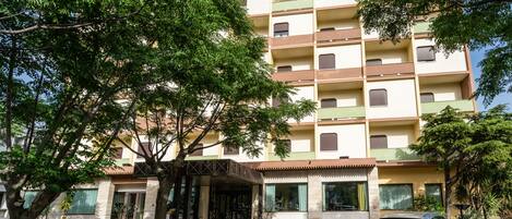Un immeuble résidentiel à plusieurs étages, doté de balcons, d’une entrée couverte et de plantes en pot.