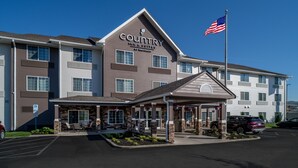 Un hôtel Country Inn & Suites doté d’une façade en pierre, d’une entrée couverte et arborant le drapeau américain.