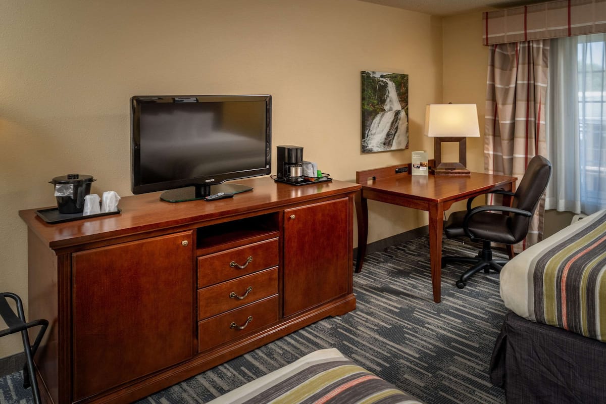A hotel room with a wooden desk, a television, a coffee maker, a lamp, a chair, and a bed with striped bedding.