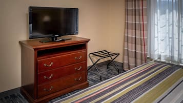 Een hotelkamer met een houten dressoir, een flatscreen televisie, een kleine zwarte stoel en een gestreept tapijt.