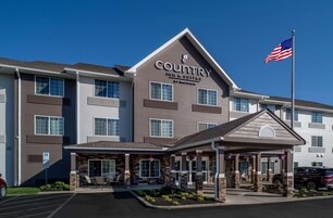 Edificio de Country Inn & Suites con fachada de piedra, una entrada cubierta y una bandera estadounidense.