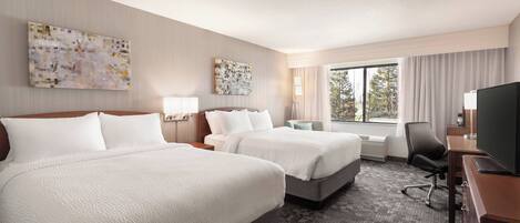 A hotel room with two beds, a desk with a flat-screen TV, a chair, and artwork on the walls.