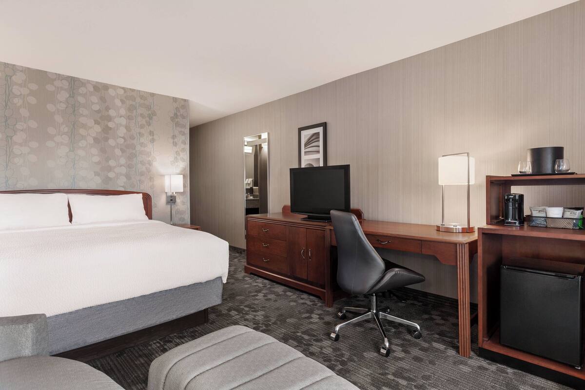 Une chambre d’hôtel équipée d’un lit, d’un bureau, d’une chaise, d’une télévision, d’une machine à café et d’un réfrigérateur.