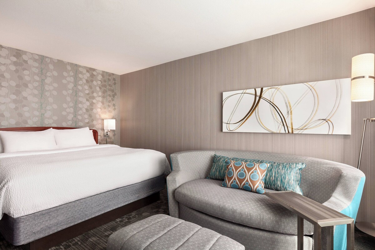 A hotel room with a bed, a sofa, a small table, and a lamp.