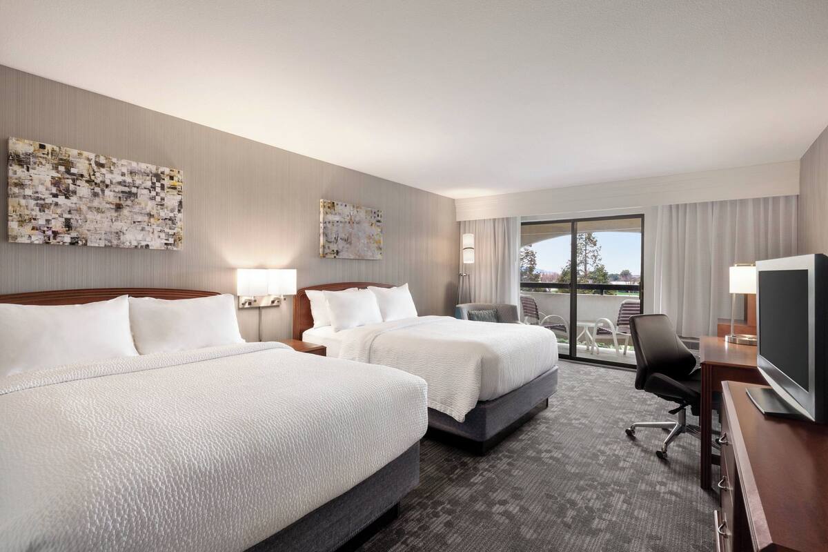 Une chambre d’hôtel avec deux lits, un bureau avec une télévision et un balcon avec des meubles d’extérieur.
