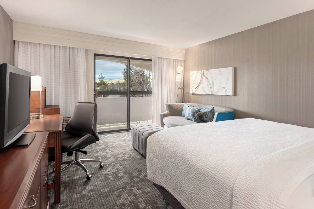 Une chambre d’hôtel avec un grand lit, un bureau avec une télévision, une chaise, un canapé et une vue sur l’extérieur grâce à une porte coulissante.