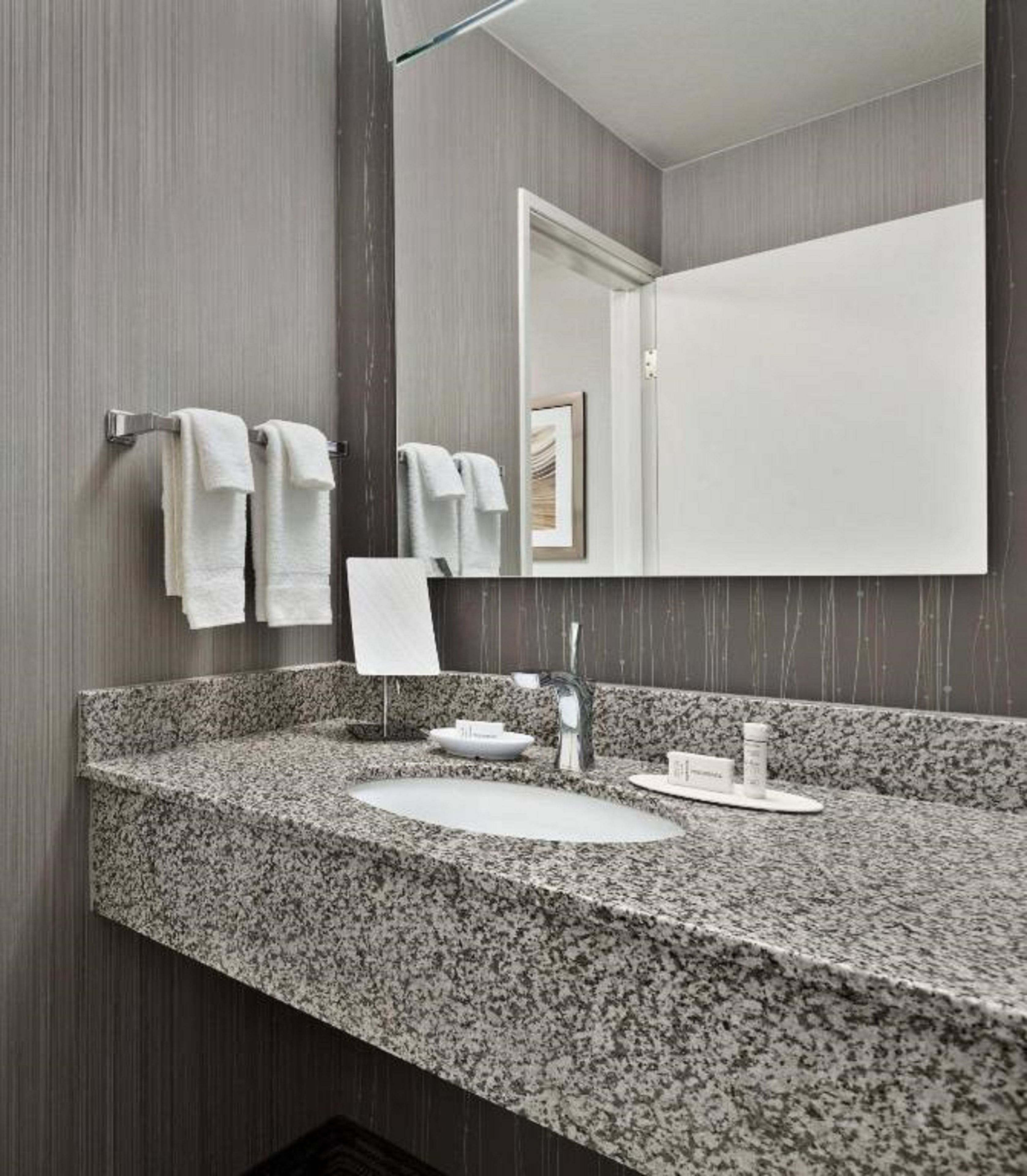 A bathroom with a granite countertop, a white sink, a mirror, and two towels hanging on a towel rack.