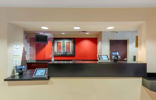Un mostrador de recepción con un quiosco digital, un televisor de pantalla plana y una pared de acento en rojo.