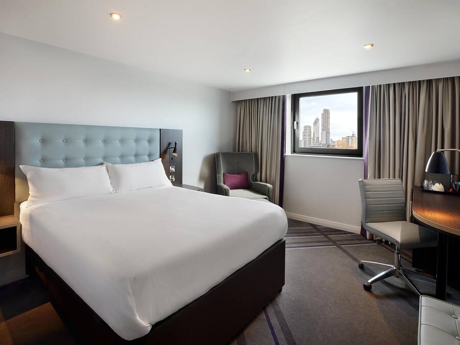 Quarto de hotel com cama grande, escrivaninha, cadeira e vista para a cidade.