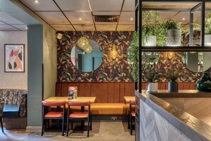 A restaurant with a booth seating area, a counter with a plant display, and a wall with a floral mural. - Premier Inn Manchester Trafford Centre Wst (Manchester)