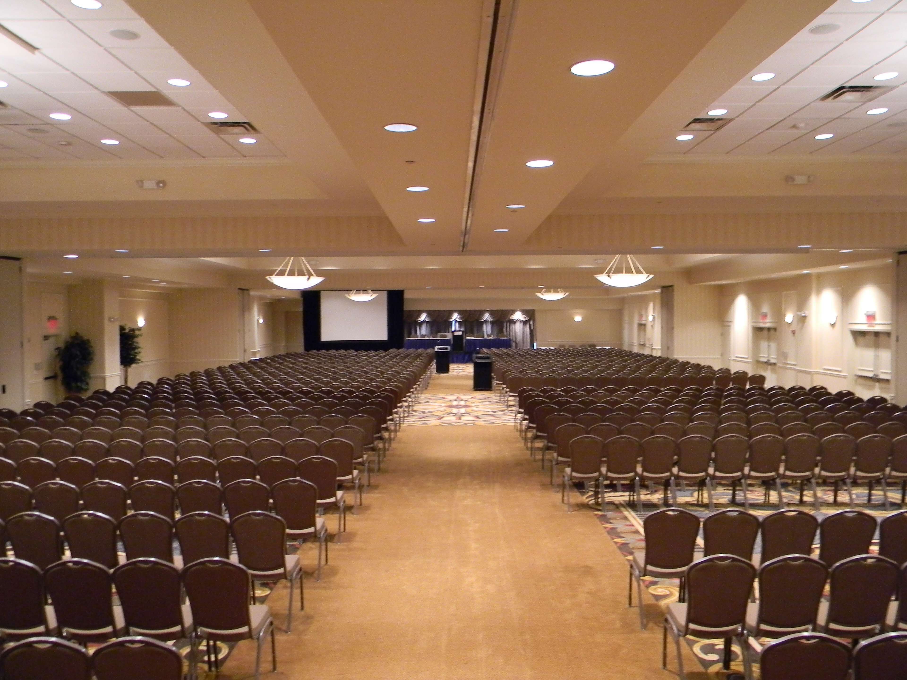Une salle de conférence avec des rangées de chaises, un pupitre et un écran à l’avant.