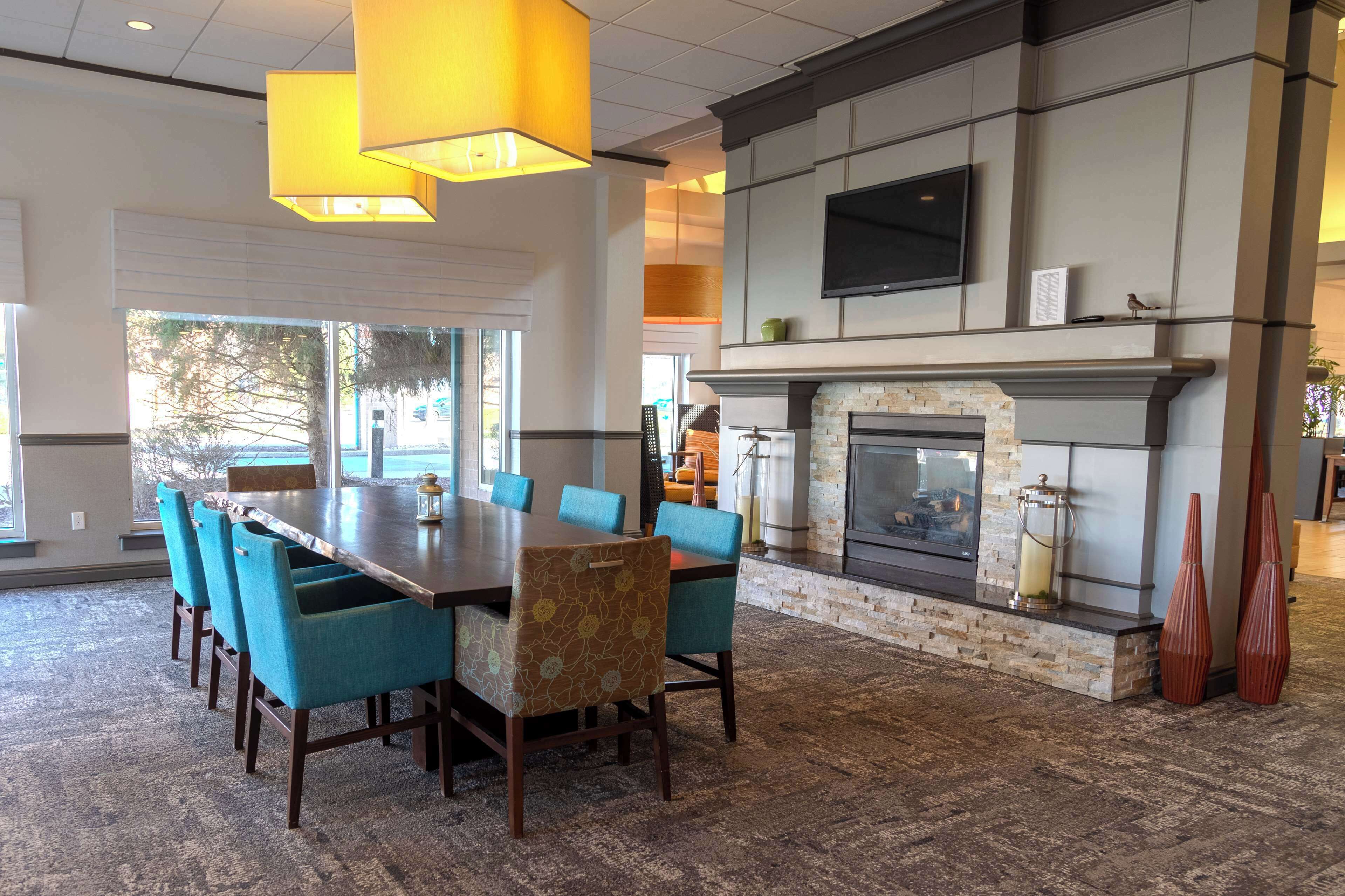 A spacious dining area with a long wooden table and blue upholstered chairs, a fireplace with a stone surround, and a flat-screen TV mounted above it.