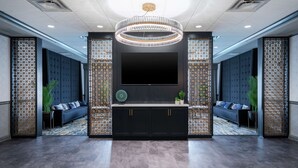 Un salon moderne doté d’un grand téléviseur, de canapés sombres, de paravents décoratifs et d’un lustre central.