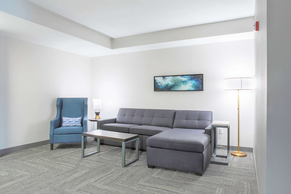 A modern living room with a sectional sofa, a blue armchair, a coffee table, a floor lamp, and a painting on the wall.