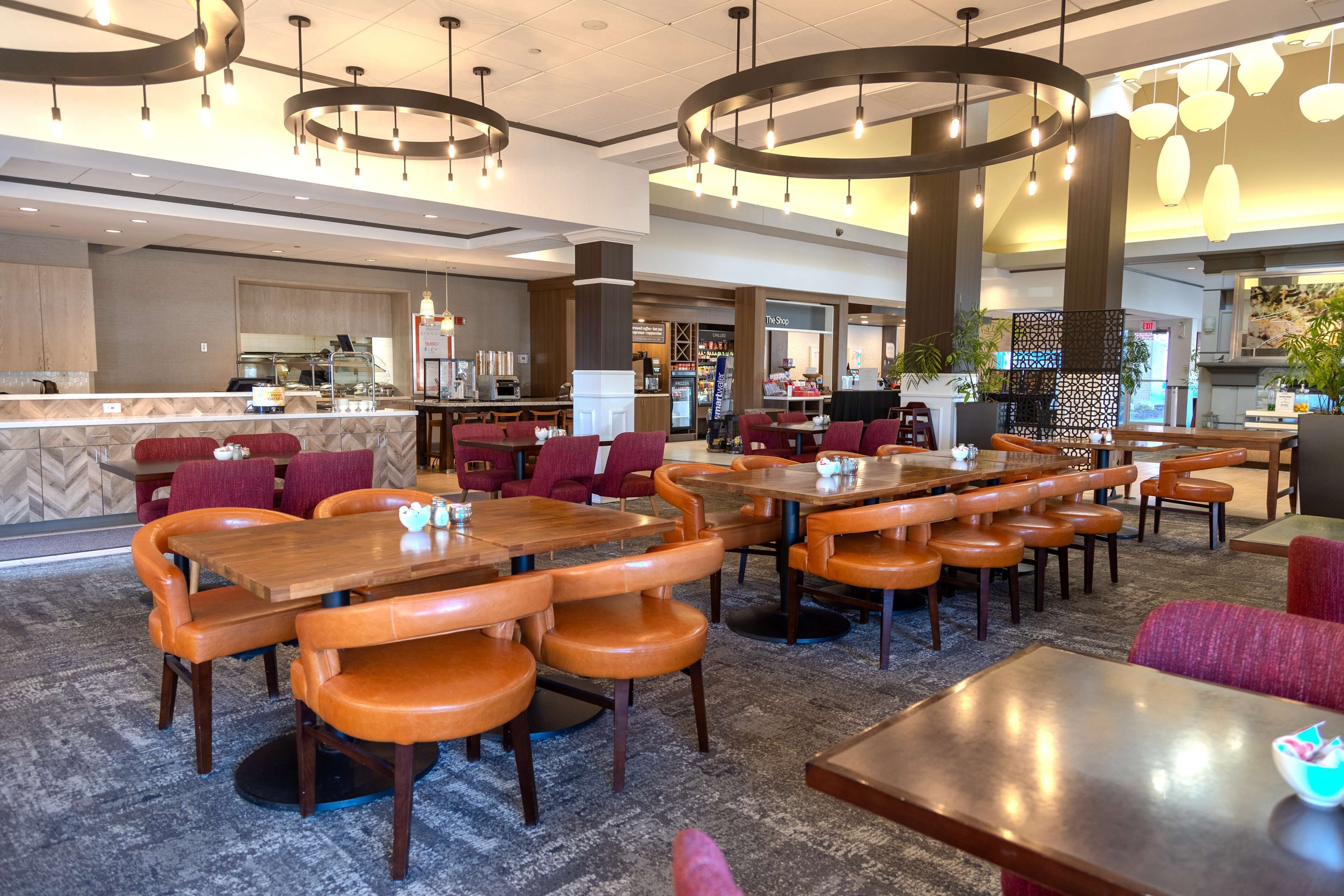 A spacious hotel lobby with multiple seating areas, a central bar, and a visible kitchen area.