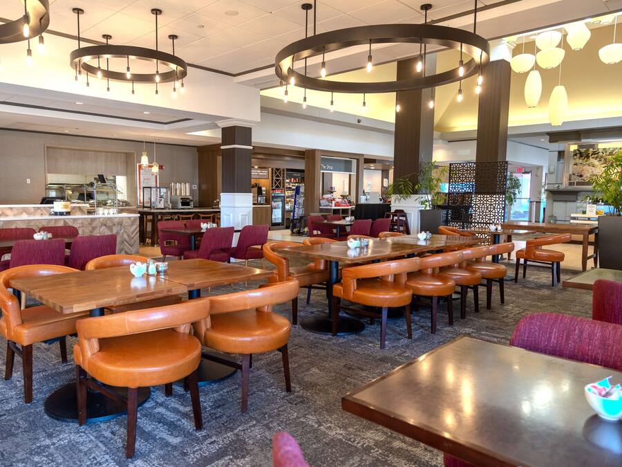 A spacious hotel lobby with multiple seating areas, a central bar, and a visible kitchen area.