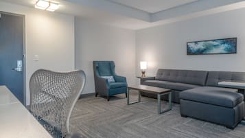 A modern hotel room with a grey sofa, a blue armchair, a wooden coffee table, and a grey carpet.