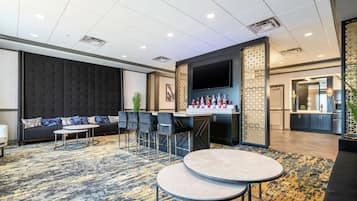 A modern hotel lobby with a bar area, seating arrangements, and a large TV screen.