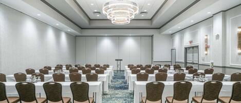 A conference room with rows of tables and chairs, a chandelier, and a carpeted floor.