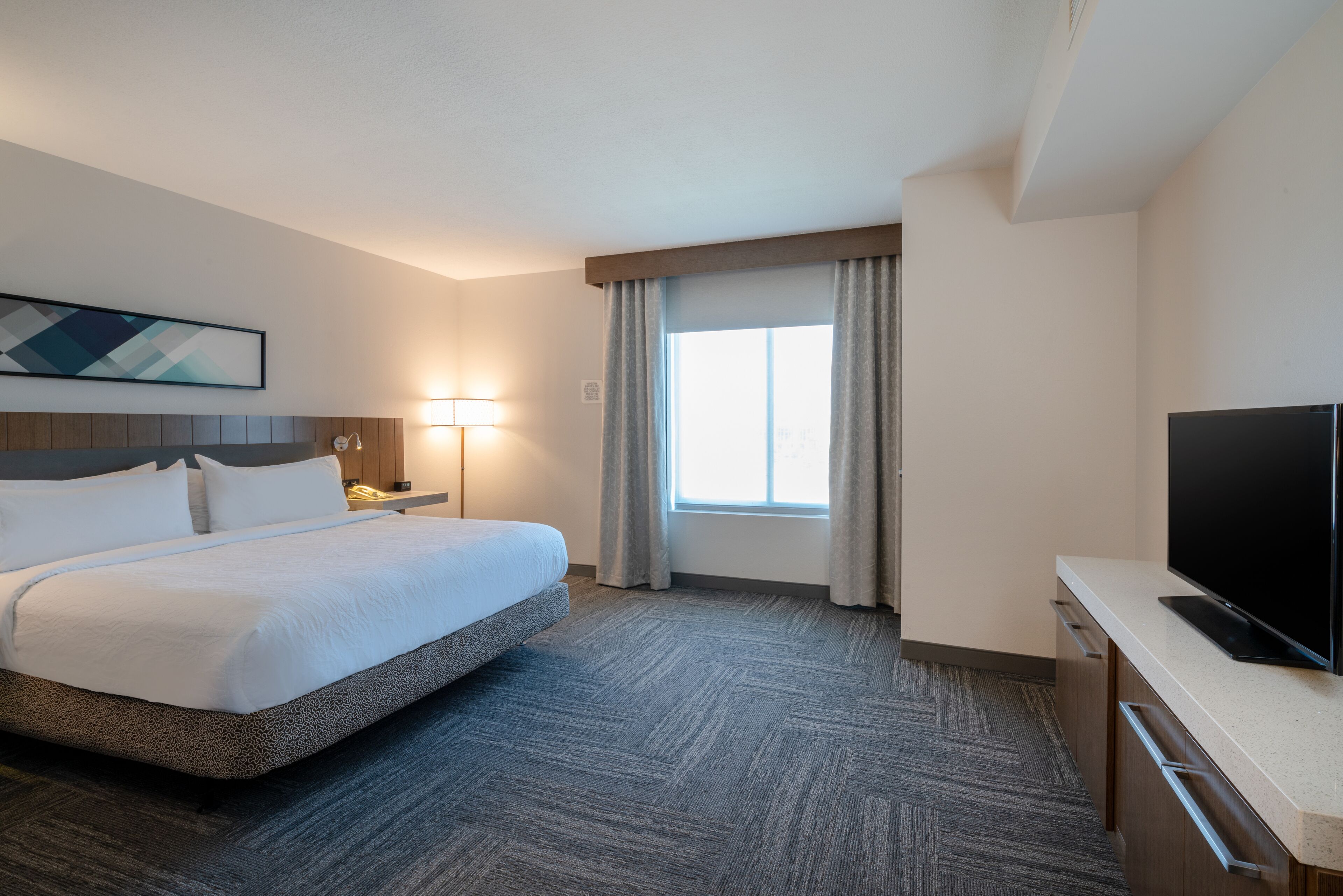 A hotel room with a large bed, a flat-screen TV, a desk, and a window with curtains.