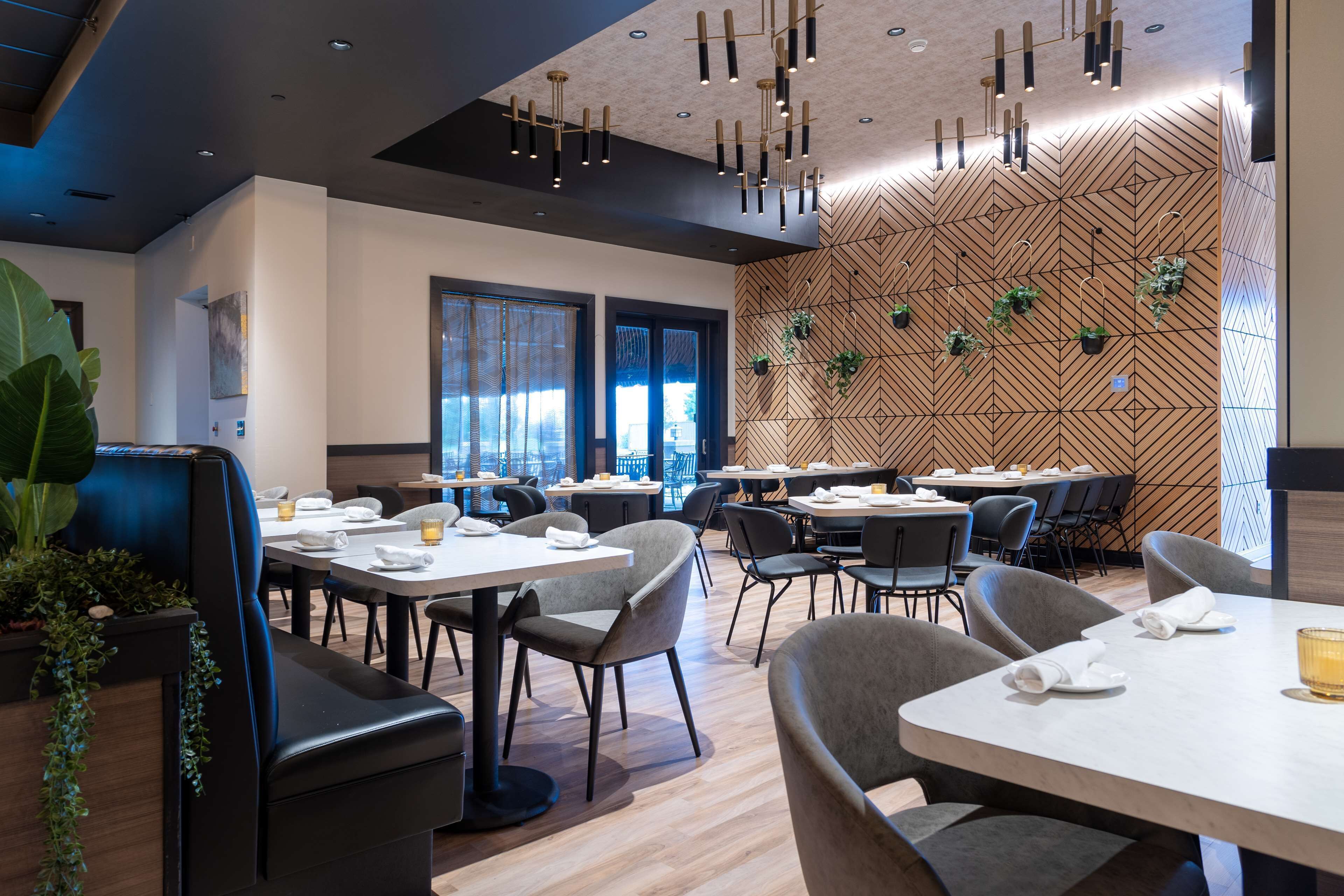 Un comedor moderno con varias mesas y sillas, paneles de madera en las paredes y plantas colgantes.