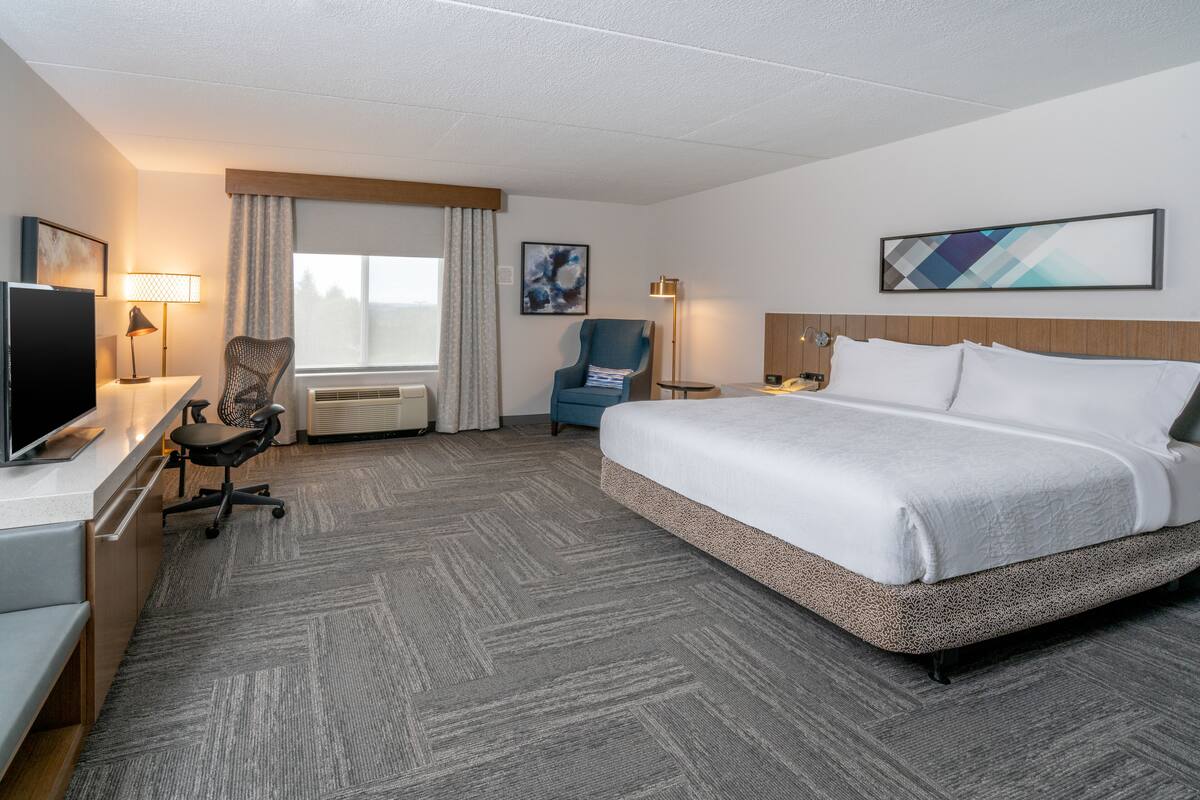 A hotel room with a large bed, a desk with a TV, a chair, a lamp, and a window with curtains.