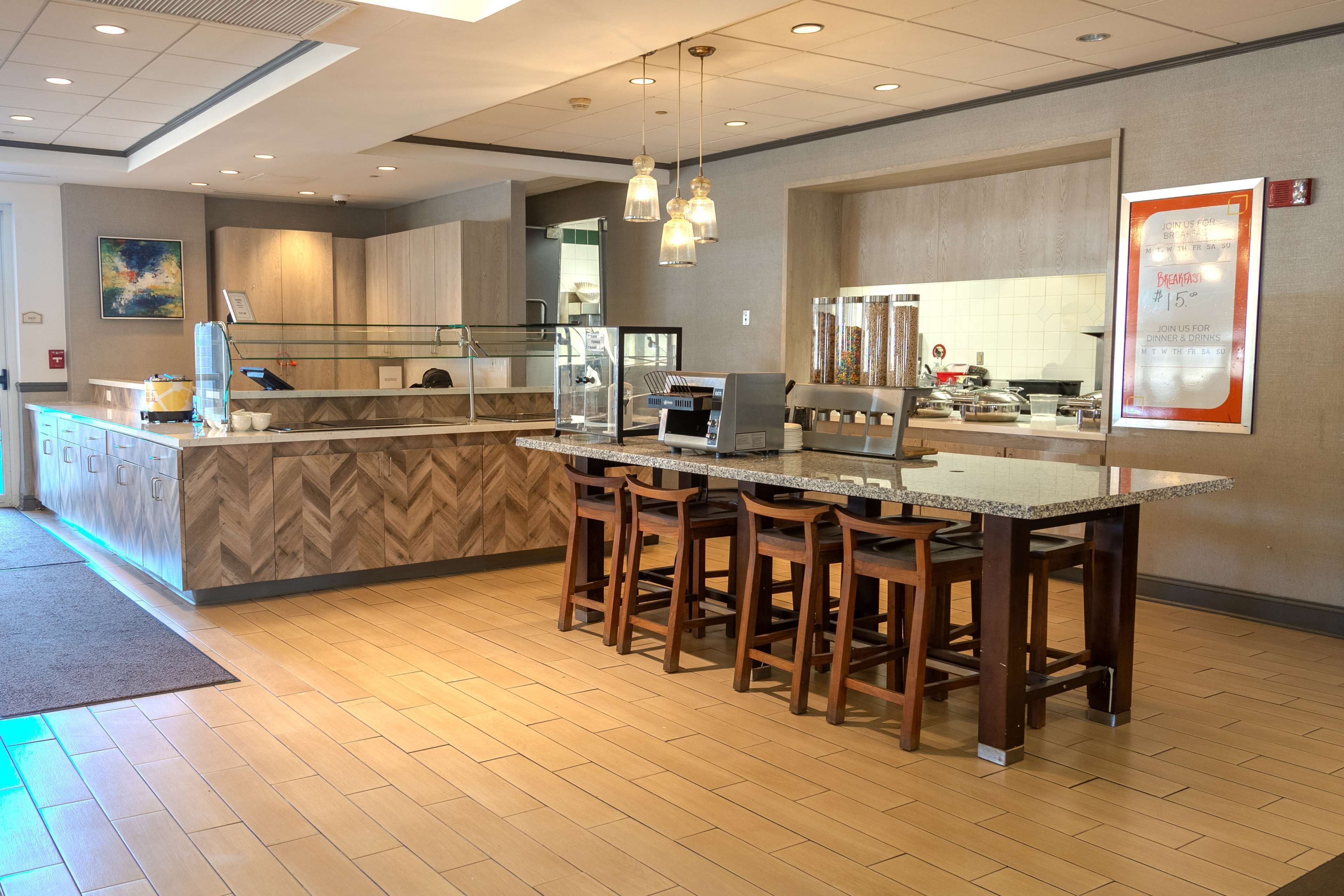 A modern kitchen area with a bar counter, wooden stools, and a coffee machine.