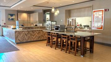 A modern kitchen area with a bar counter, wooden stools, and a coffee machine.