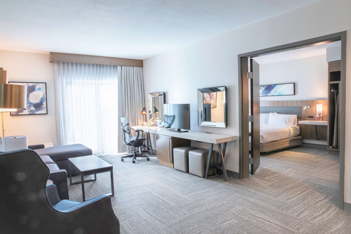 A modern hotel room with a large bed, a desk with a computer, a chair, and a sofa.
