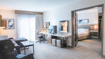 A modern hotel room with a large bed, a desk with a computer, a chair, and a sofa.