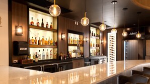Un espace bar doté d’un comptoir en marbre poli, de nombreuses bouteilles d’alcool et de luminaires sphériques suspendus.
