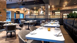Un intérieur de restaurant moderne, avec de nombreuses tables et chaises, un bar et un espace détente doté de bancs rembourrés.