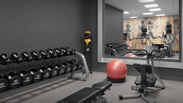 A gym with dumbbells, a stationary bike, a treadmill, and a red exercise ball.