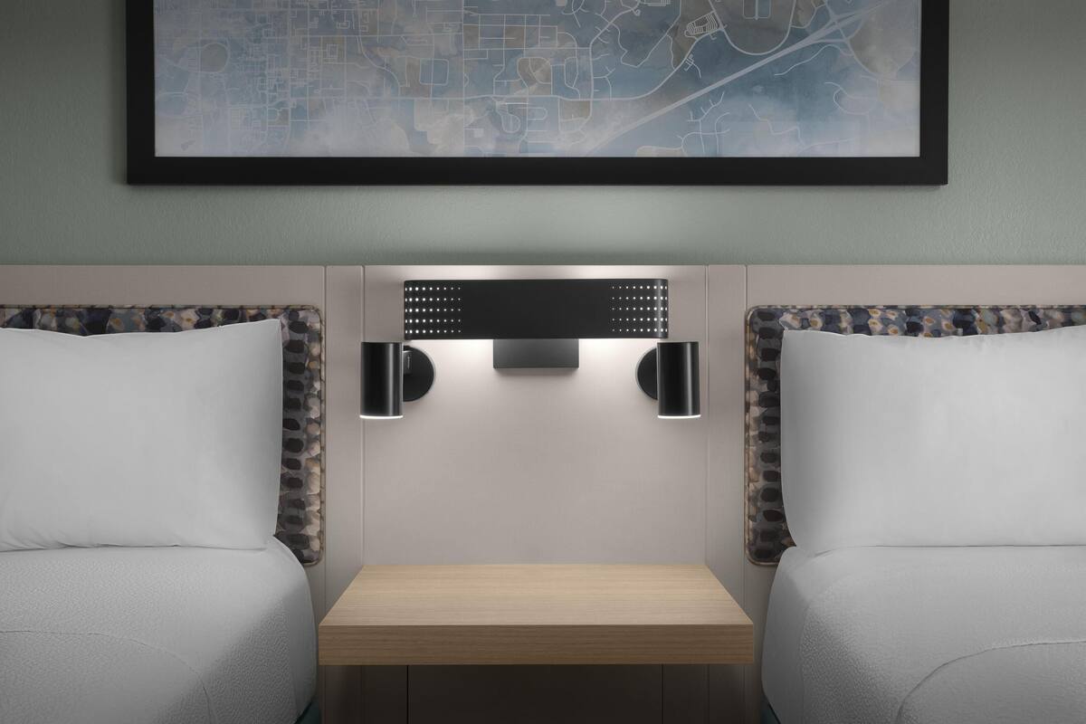 Une chambre d’hôtel avec deux lits, une petite table en bois et des lampes fixées au mur.