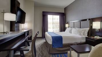 A hotel room with a bed, desk, chair, TV, and a window with curtains.